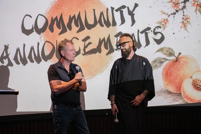 More community announcements roll on — mic handoffs and short stage spots — A beat later in the same beat.