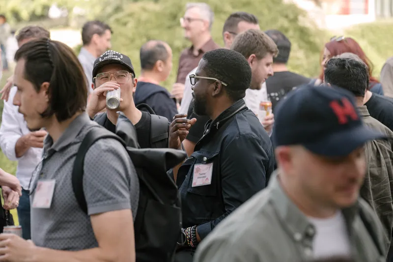Crowds fill the courtyard for outdoor networking in the late-day light — Wider angle.