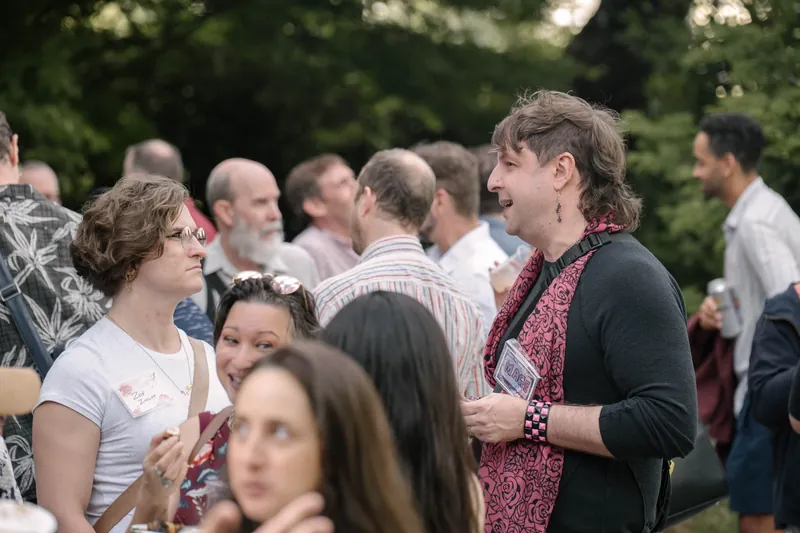 Crowds fill the courtyard for outdoor networking in the late-day light — Audience heads in the foreground.