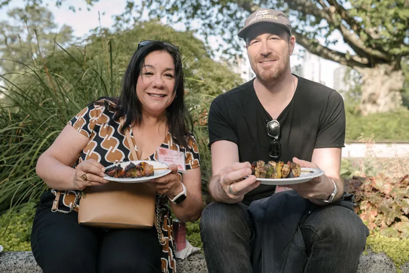 Guests smile for the camera with plates of BBQ on the outdoor patio — From the aisle.