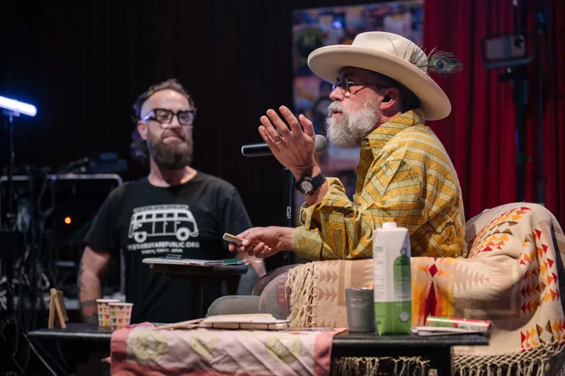 Dave Olson leans into the mic during the on-stage conversation, peacock feather in his hatband.