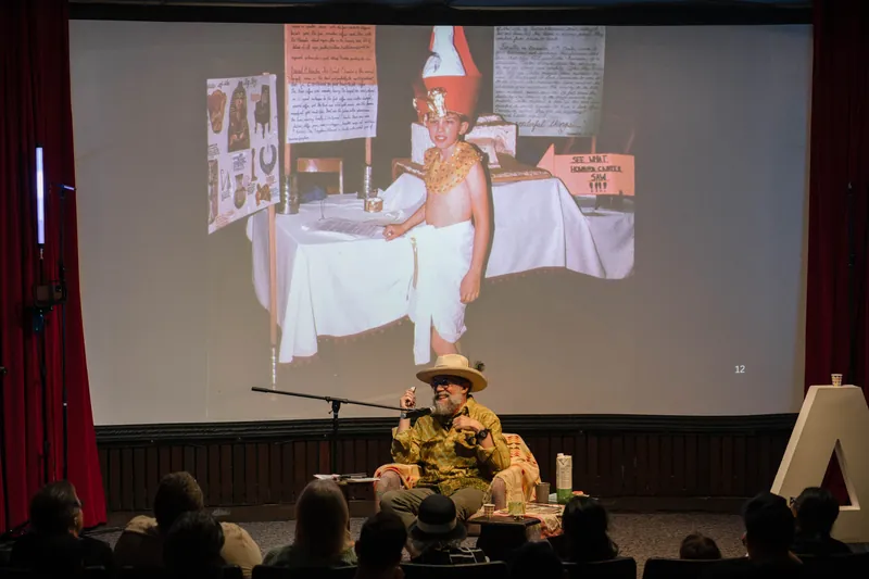 Dave Olson speaks from the armchair, gesturing as slides cycle behind him — Tight frame.