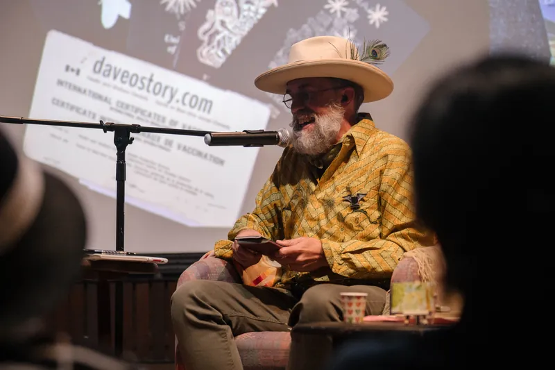 Dave Olson continues from the armchair as denser text and photo slides roll — Stage-left view.
