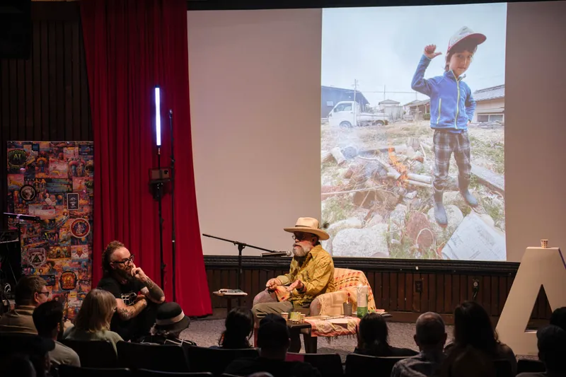 An on-stage conversation with Dave Olson — two chairs, mic, and a listening room — Screen bright in the background.