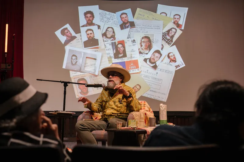 Dave Olson leans into storytelling — clippings, collages, and handwritten notes on screen — Stage-left view.