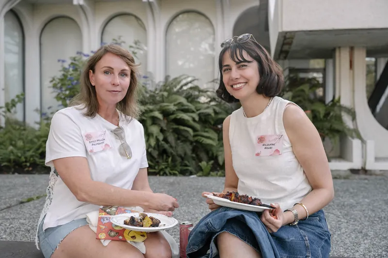 Guests smile for the camera with plates of BBQ on the outdoor patio — Wider angle.