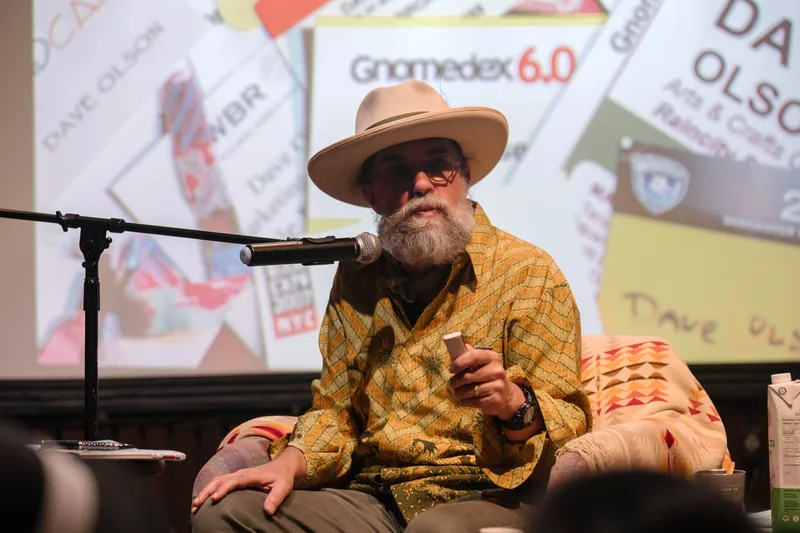 Dave Olson continues from the armchair as denser text and photo slides roll — Closer on the mic.