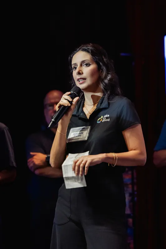 A presenter holds notes at the microphone during the project overview.