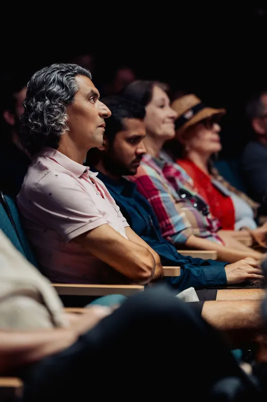 Audience members sit in a row and listen to the stage presentation.