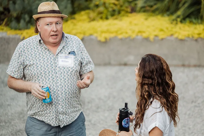 An attendee in a straw hat chats with another guest in the garden.