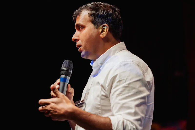 Taleeb Noormohamed explains a point with both hands near the microphone.
