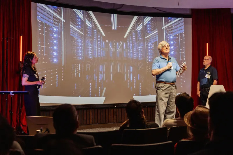 The Data for Good team presents beside an image of illuminated data servers.