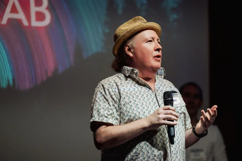A community presenter speaks from the stage in a close front view.