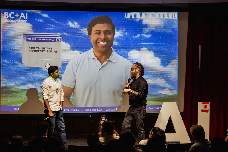 Taleeb Noormohamed and the host meet onstage beneath the event slide.