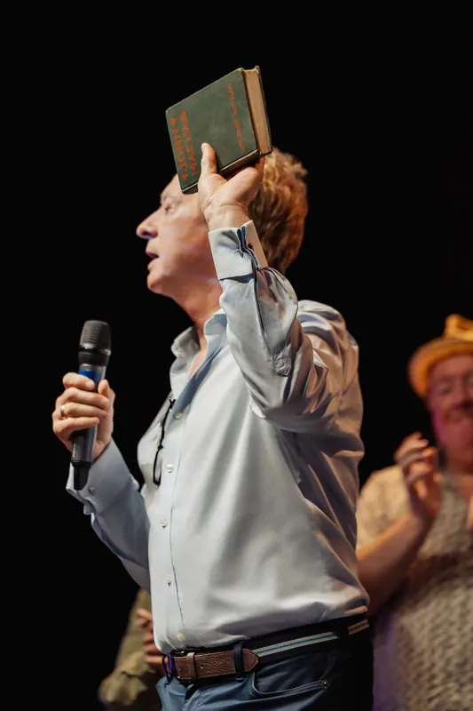 A community presenter raises a small book over his head.