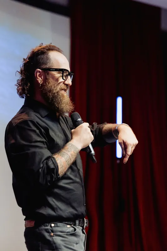 The host checks a wristwatch while speaking into the microphone.