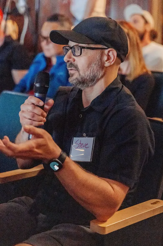 An audience member in a cap asks a question with a handheld microphone.