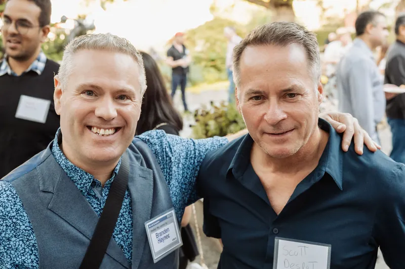 Two attendees smile with their arms around one another at the reception.