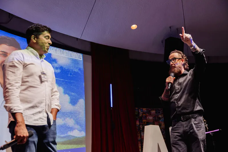 The host points upward while Taleeb Noormohamed looks on.