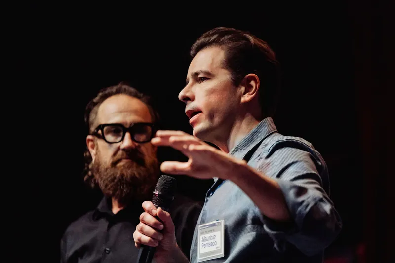 A community presenter describes an idea with a broad hand gesture beside the host.