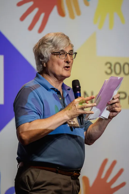 A presenter holds up printed notes while addressing the audience.