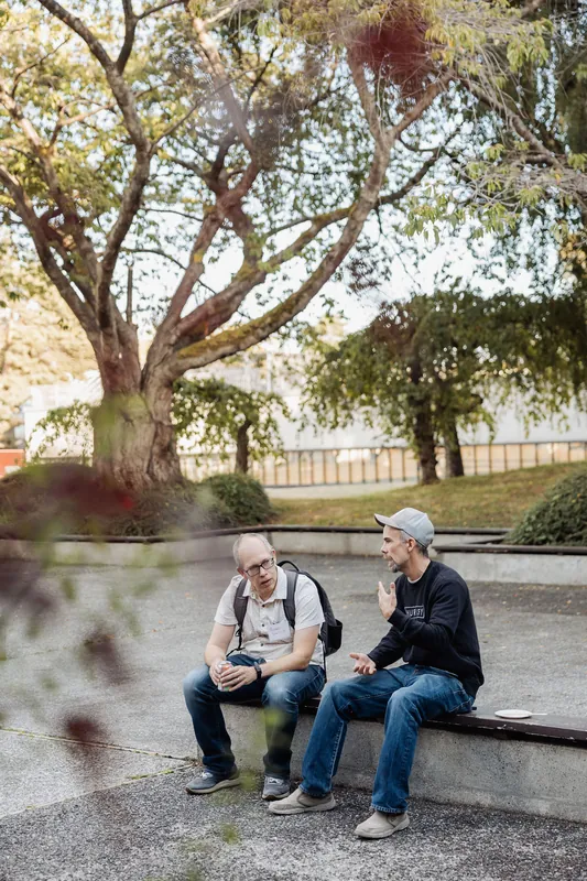 A wide garden view frames two attendees talking beneath a tree.