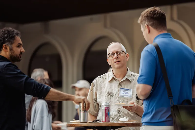 Three attendees exchange greetings around a patio table.