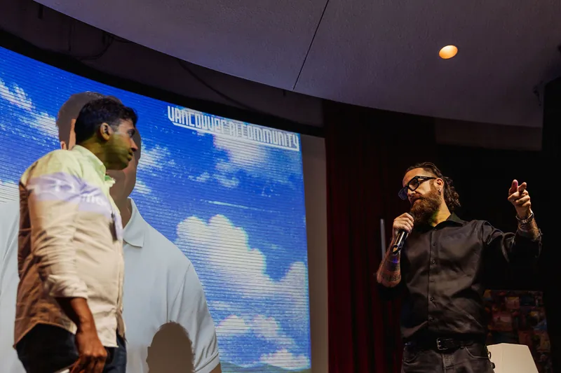 The host addresses Taleeb Noormohamed in front of the projected event portrait.