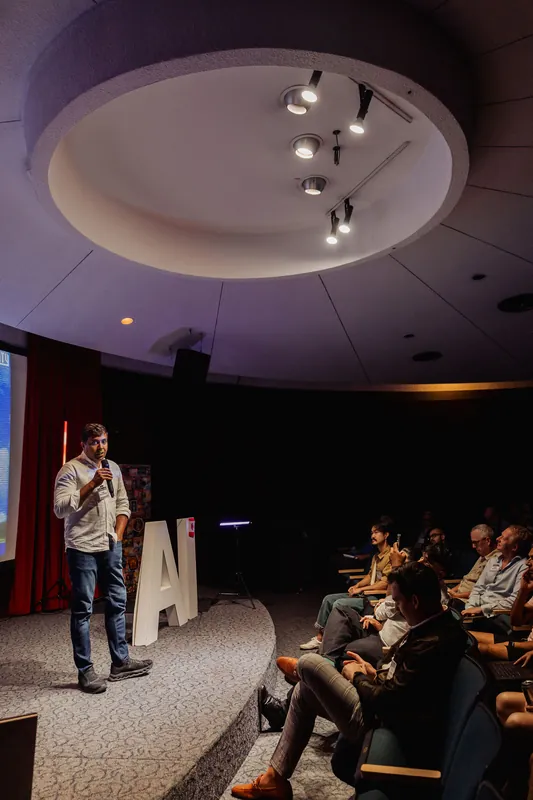 A wide view shows Taleeb Noormohamed addressing the seated audience.