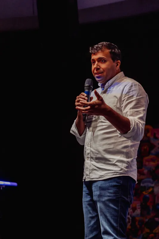 Taleeb Noormohamed gestures toward the room while holding the microphone.