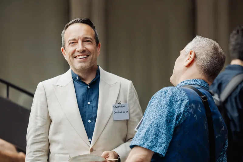 An attendee in a light blazer smiles during a reception conversation.