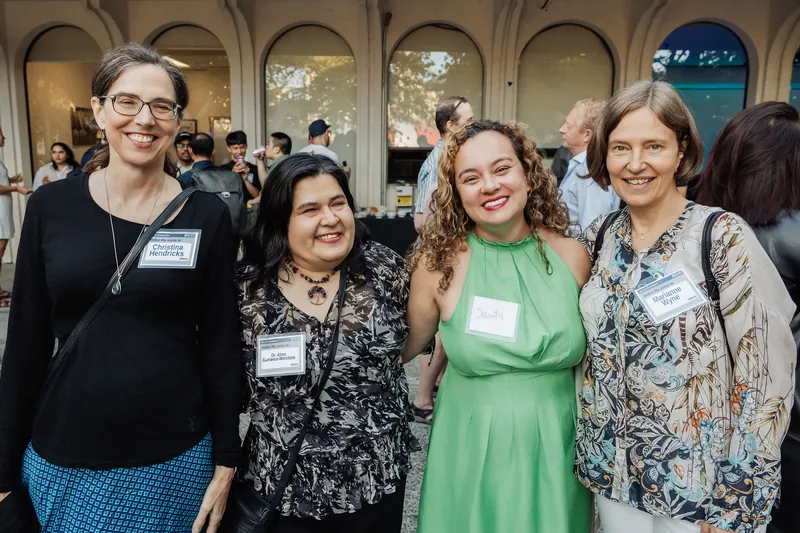 Four attendees smile for a group portrait with the reception behind them.