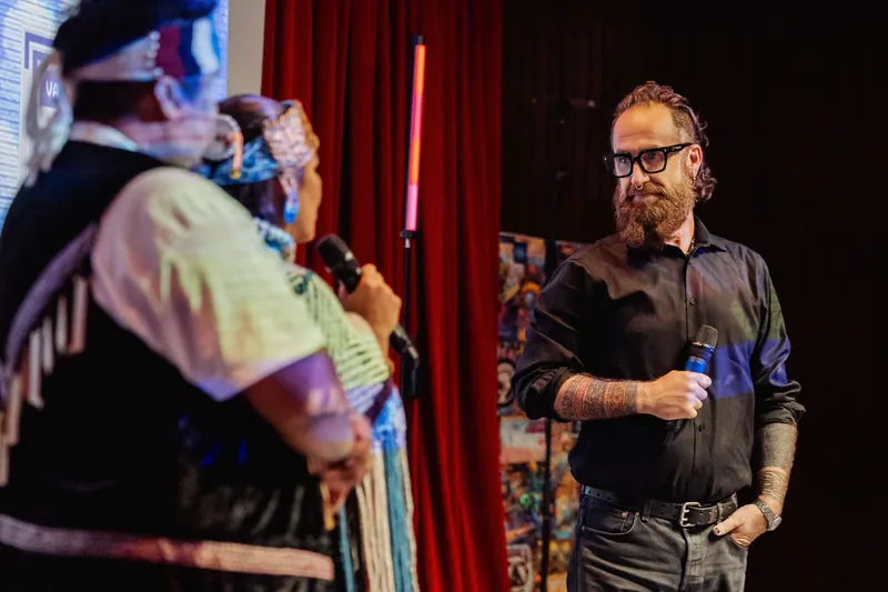 A cultural representative listens as the host speaks into the microphone.
