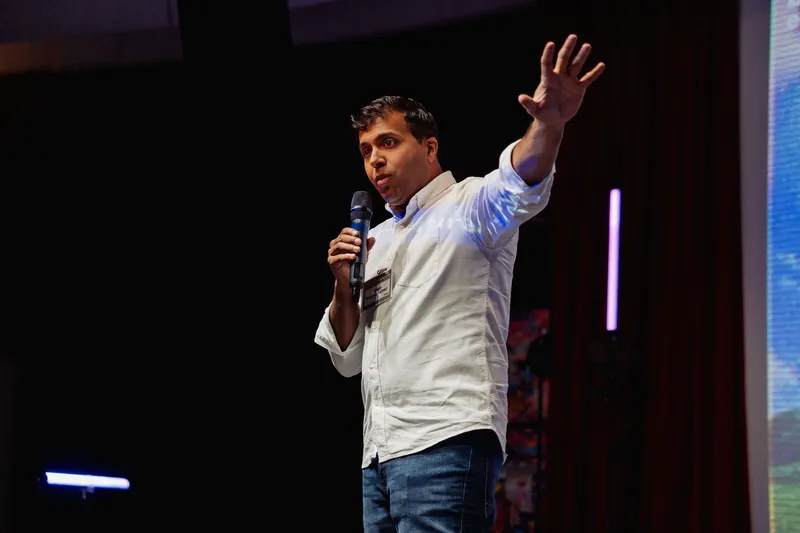 Taleeb Noormohamed raises one arm high while addressing the audience.
