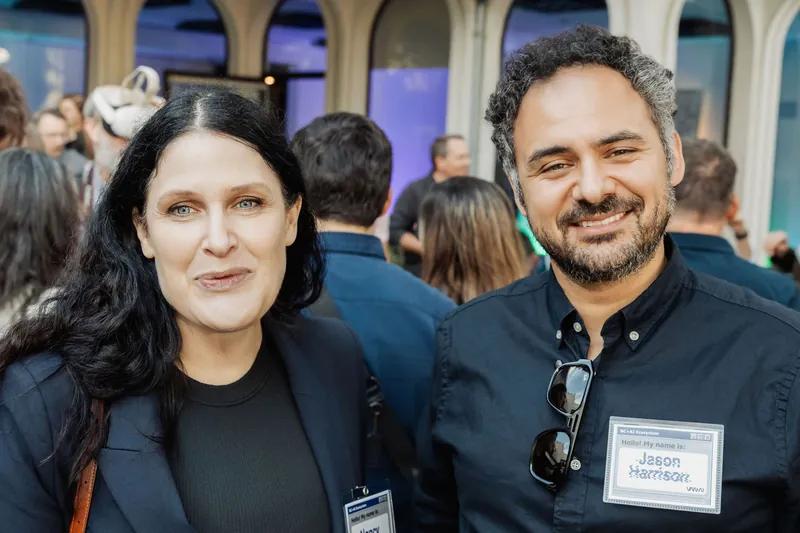 Two attendees pose for a close portrait in front of the reception crowd.