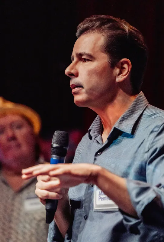 A community presenter points forward while speaking from the stage.