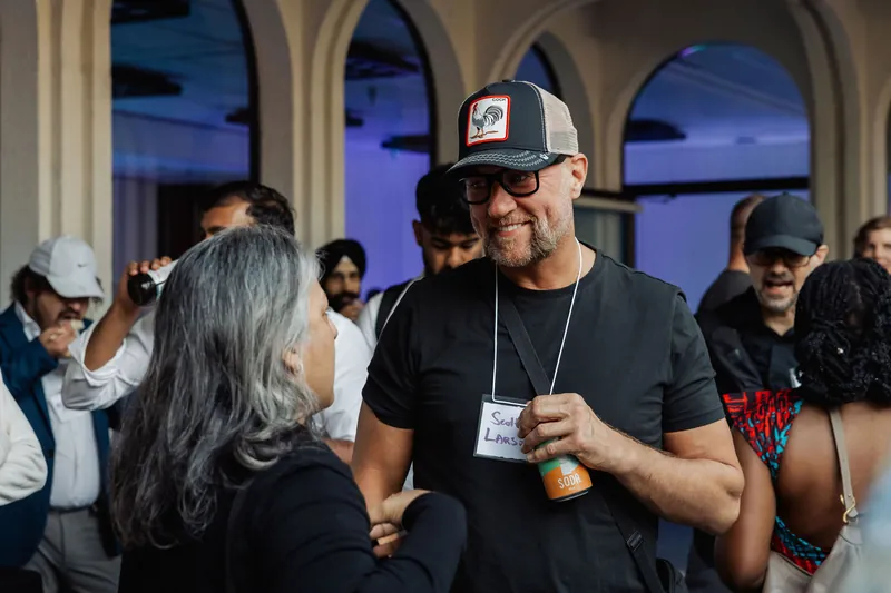 An attendee in a black cap smiles while talking in the crowd.