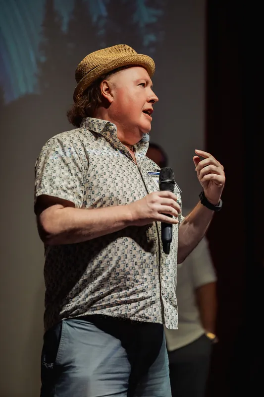 A presenter raises one hand while explaining a community initiative.
