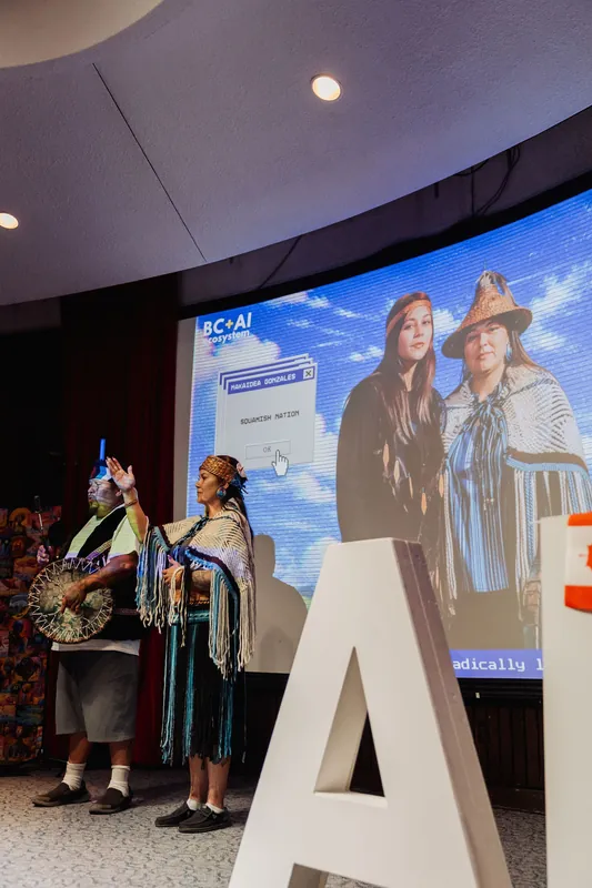 The two cultural representatives stand before a projected portrait of themselves.