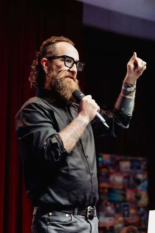 The host lifts both hands while addressing the audience.