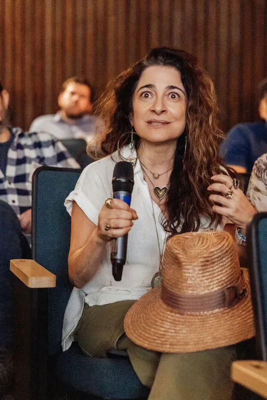 A seated attendee holds a microphone while addressing the stage.