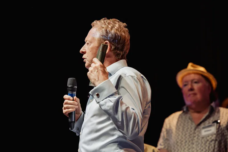 A presenter displays a book beside his face during an onstage announcement.