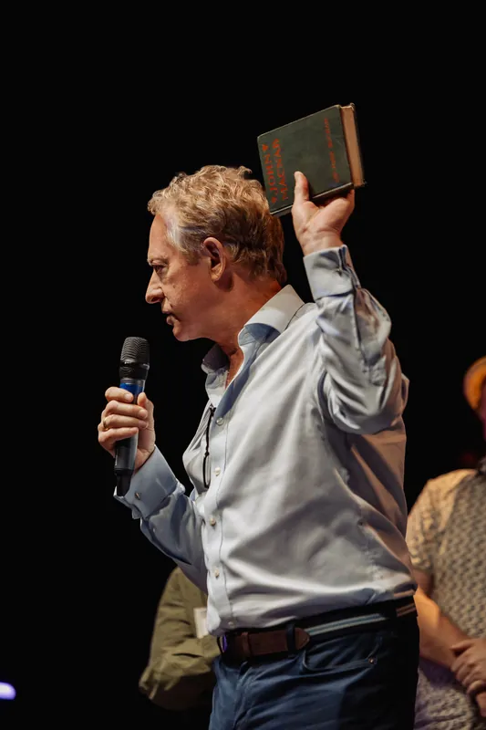 A presenter holds a book overhead in a close side view.