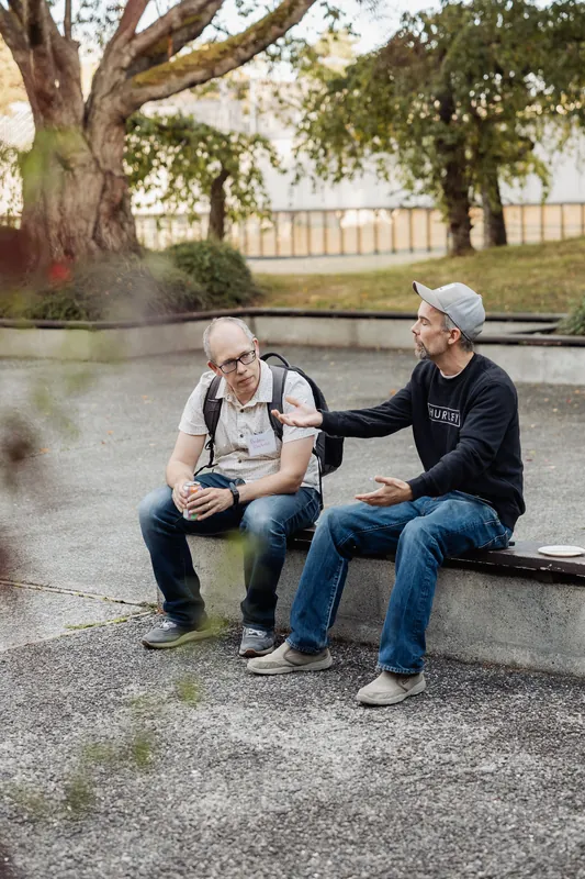 Two attendees sit on a low wall and talk in the garden.