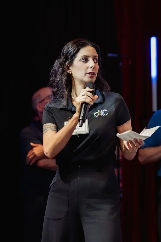 A close detail frames a presenter's microphone, notes, and Data for Good shirt.