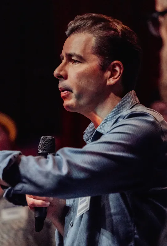 A community presenter speaks into a microphone in a close side portrait.