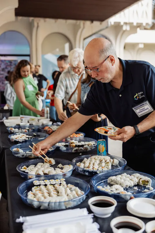 A person serves food while attendees gather around the buffet.