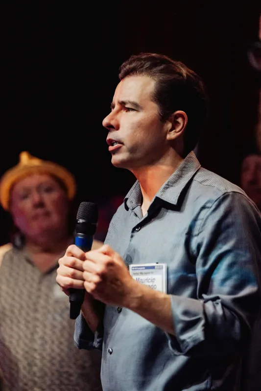 A community presenter pauses with the microphone held at chest height.