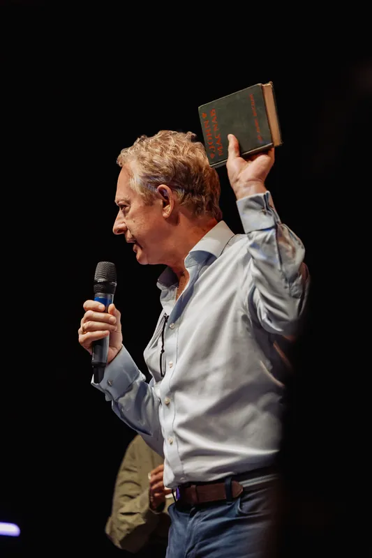 A presenter smiles while holding a book aloft onstage.