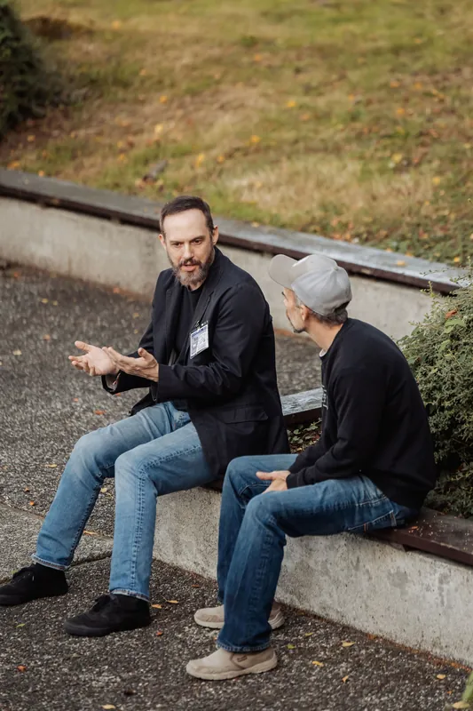 Two attendees sit on a low wall and have an animated conversation.